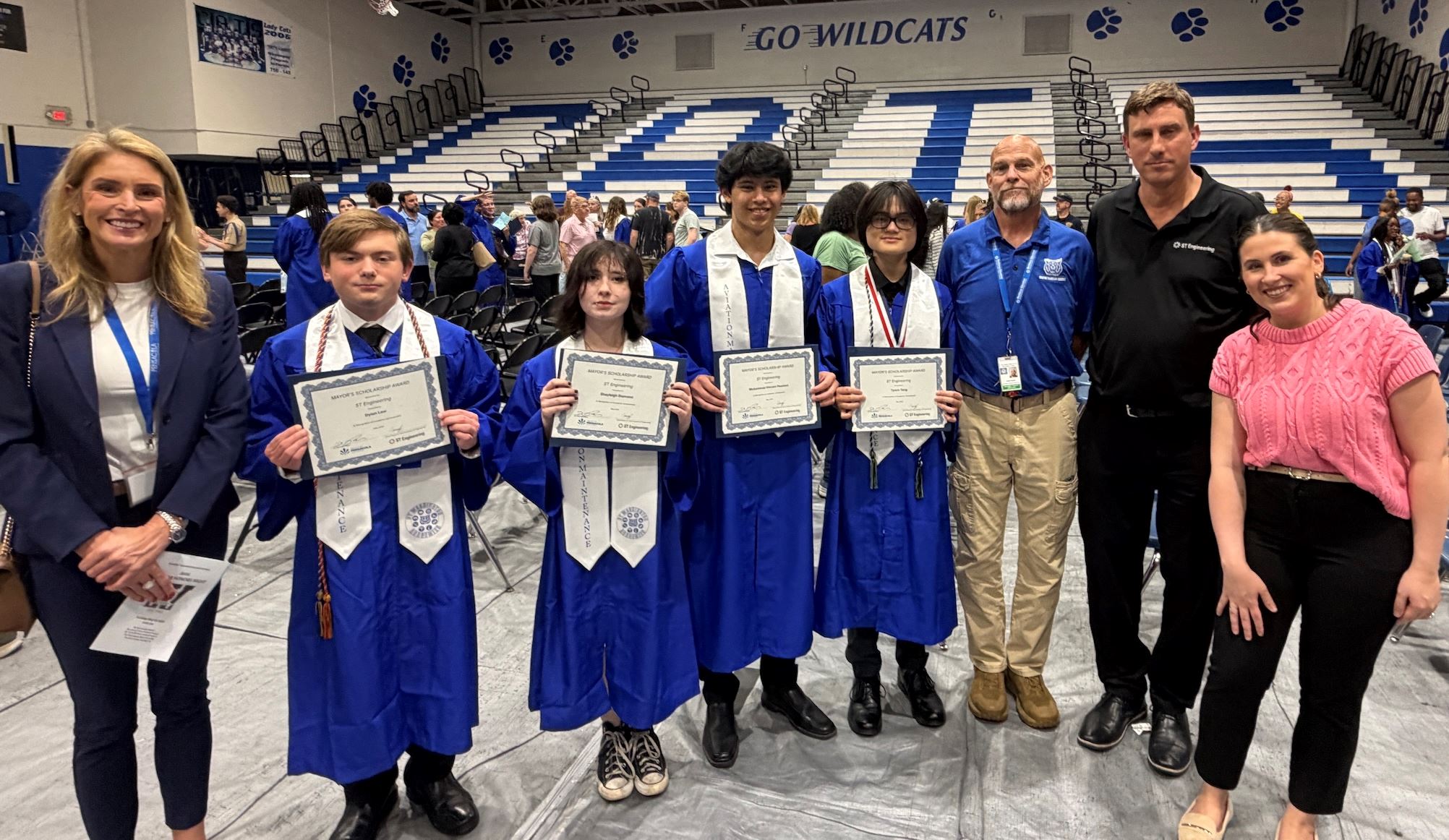 Graduates holding scholarship certificates in school gym
