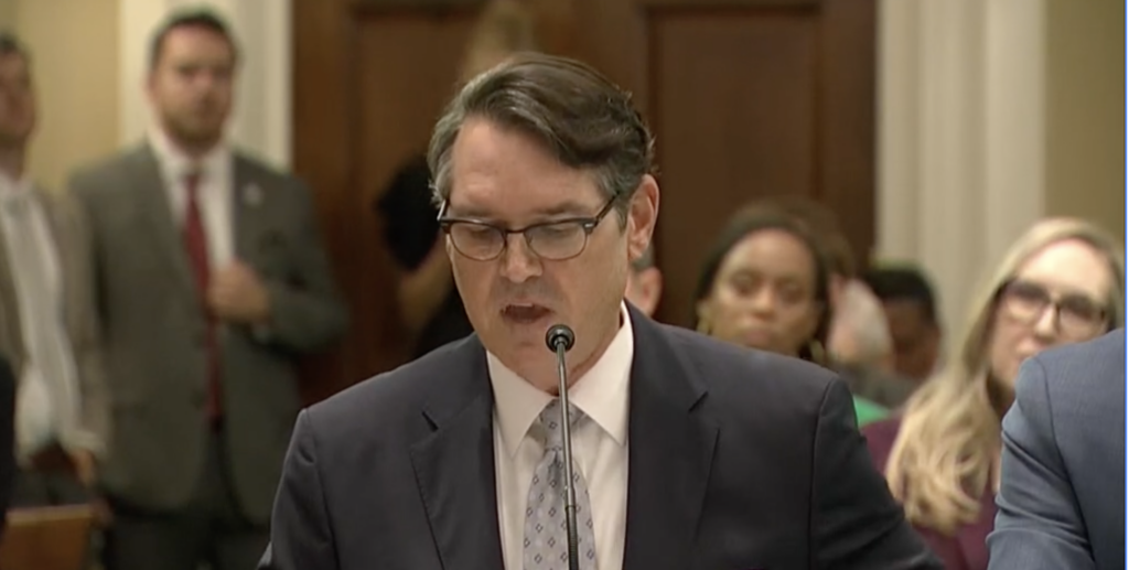 Man in suit speaking at formal hearing