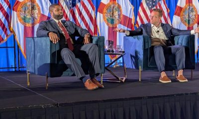 Two men speaking on stage with flags