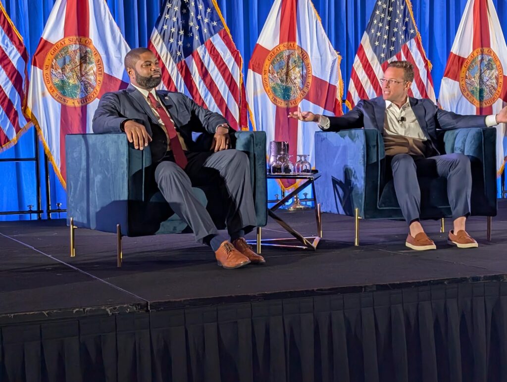 Two men speaking on stage with flags