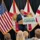 Man speaking at podium with Florida flags