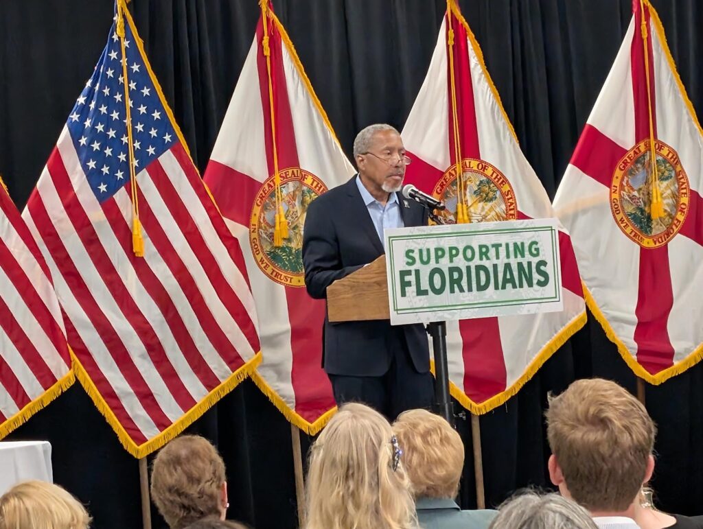 Man speaking at podium with Florida flags