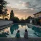 Two children sitting by backyard pool at sunset