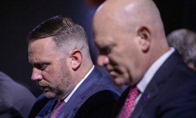 Two suited men with heads bowed solemnly
