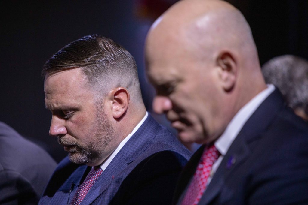 Two suited men with heads bowed solemnly