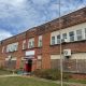 Boarded-up brick school building with red entrance