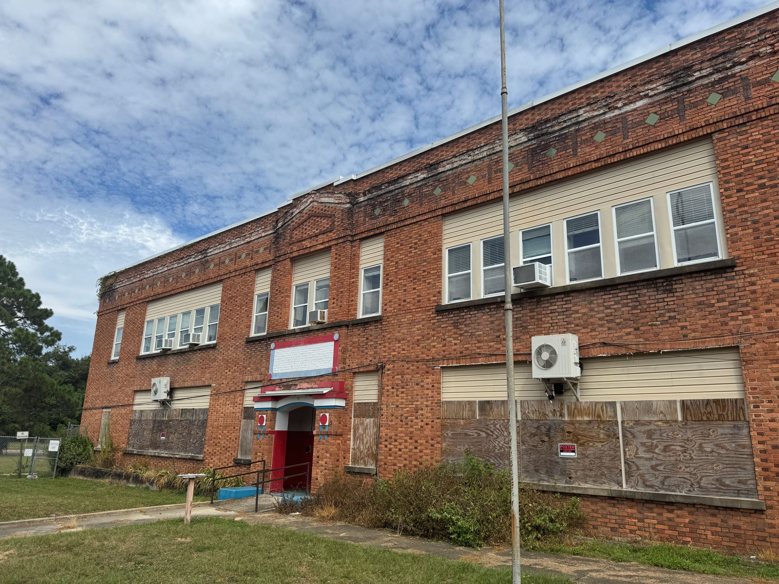 Boarded-up brick school building with red entrance