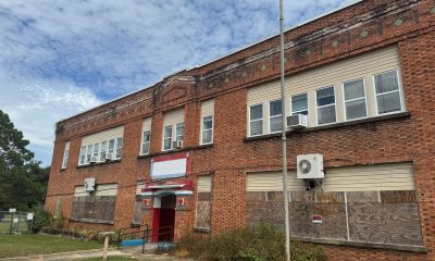 Boarded-up two-story brick building with red entrance