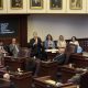 Lawmakers debate in legislative chamber with vote board