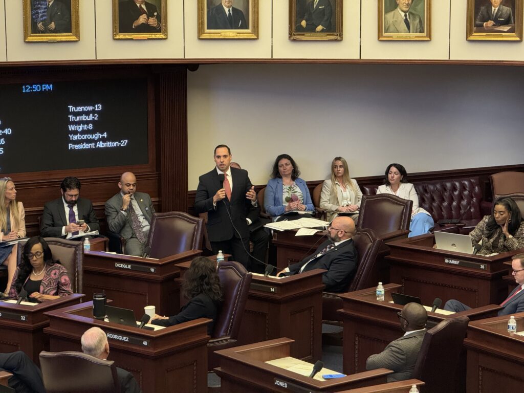 Lawmakers debate in legislative chamber with vote board