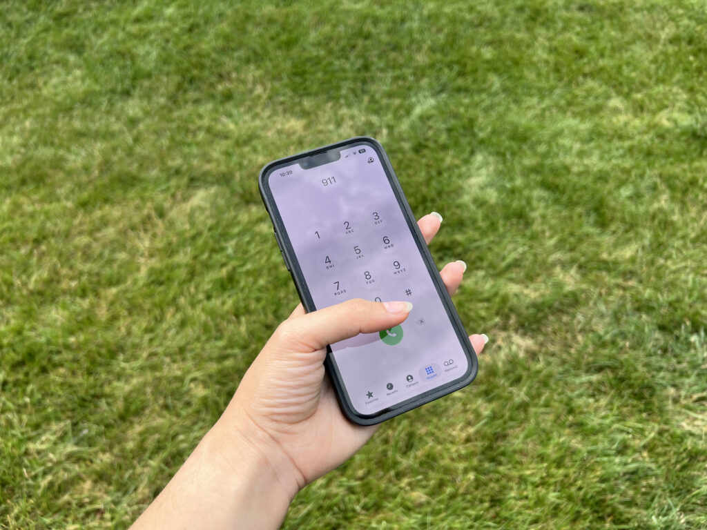Hand dialing 911 on smartphone outdoors