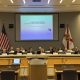 Government panel meeting with presentation and flags