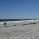 People walking along sunny ocean beach shoreline
