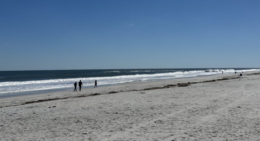 People walking along sunny ocean beach shoreline
