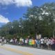 Protesters holding signs along roadside under blue sky