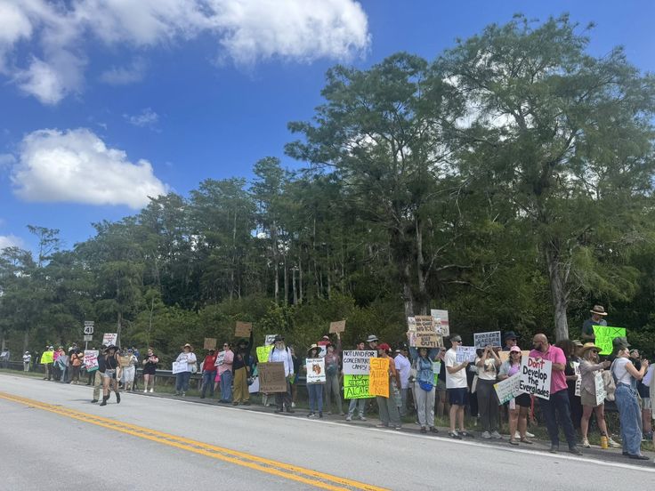 Protesters holding signs along roadside under blue sky