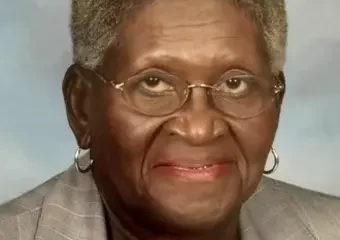 Elderly woman wearing glasses and gray blazer