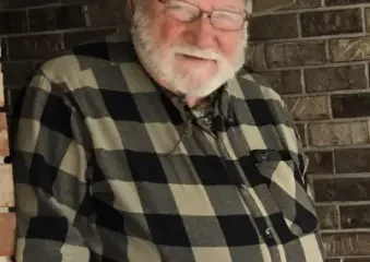 Older man in hat smiling by brick wall