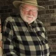 Older man in hat smiling by brick wall