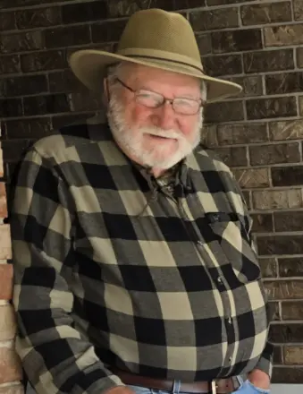 Older man in hat smiling by brick wall