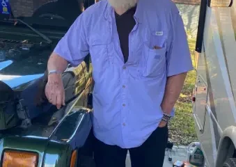 Bearded man leaning on green Jeep in driveway