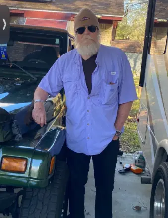Bearded man leaning on green Jeep in driveway