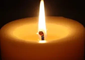 Lit candle with glowing flame in darkness