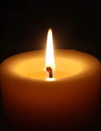 Lit candle with glowing flame in darkness
