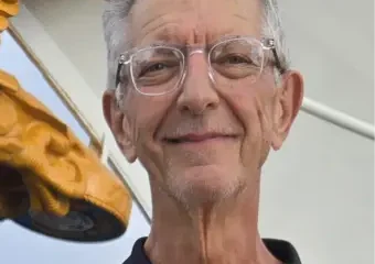 Older man with glasses beside golden wing sculpture