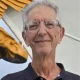 Older man with glasses beside golden wing sculpture