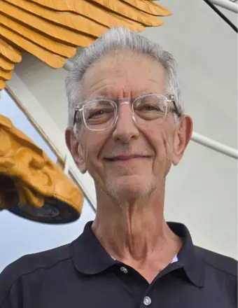 Older man with glasses beside golden wing sculpture