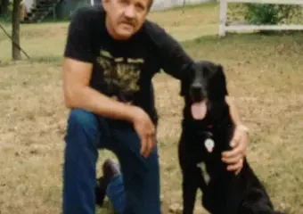 Man kneeling beside black dog in yard