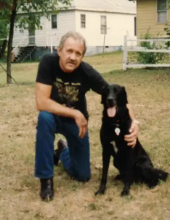 Man kneeling beside black dog in yard