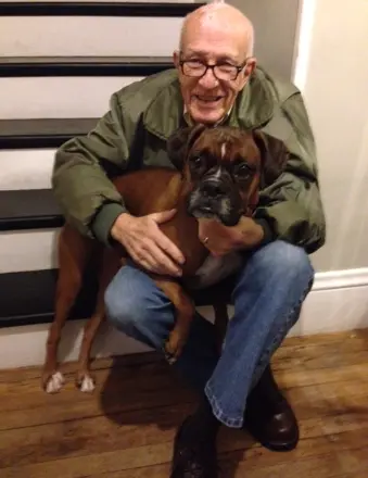 Elderly man hugging brown boxer dog indoors