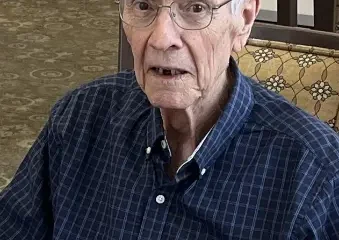 Elderly man wearing glasses and plaid shirt indoors