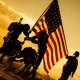 Soldiers raising American flag at sunset silhouette