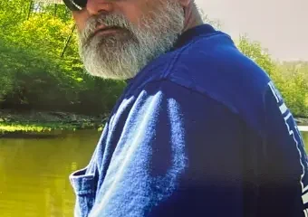 Bearded man fishing by riverside wearing straw hat