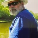 Bearded man fishing by riverside wearing straw hat