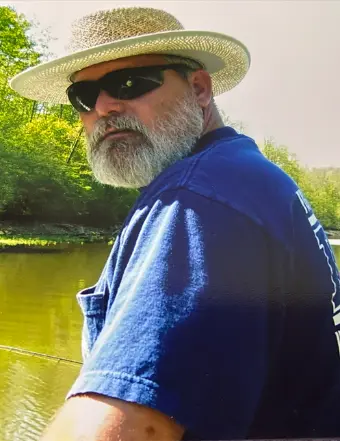 Bearded man fishing by riverside wearing straw hat