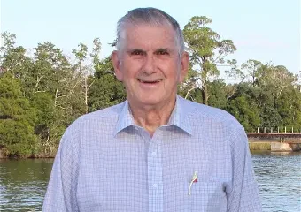 Elderly man standing by riverside with trees