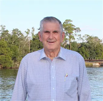 Elderly man standing by riverside with trees