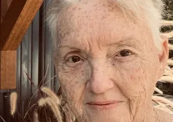 Elderly woman with glasses outdoors near wooden wall