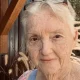 Elderly woman with glasses outdoors near wooden wall