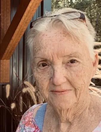 Elderly woman with glasses outdoors near wooden wall