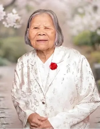 Elderly woman in floral attire with red flower