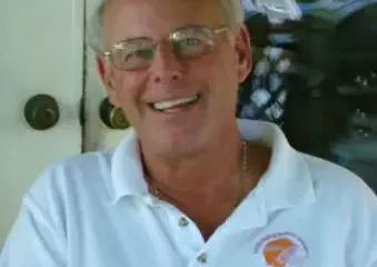 Smiling older man wearing glasses and white polo