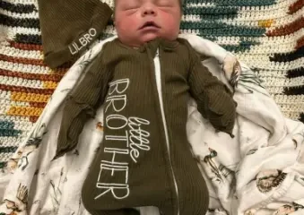Sleeping newborn in green 'little brother' onesie