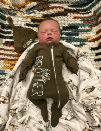 Sleeping newborn in green 'little brother' onesie