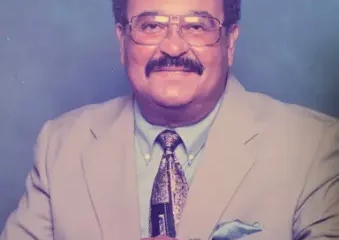 Man in beige suit with glasses smiling