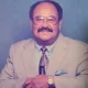 Man in beige suit with glasses smiling